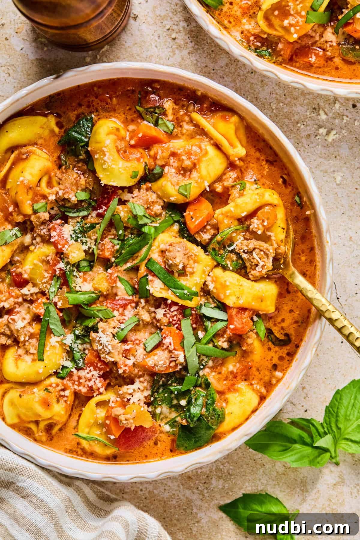 Slow-Cooker Sausage and Tortellini Soup Recipe 2 Bowl with sausage tortellini soup topped with fresh basil.