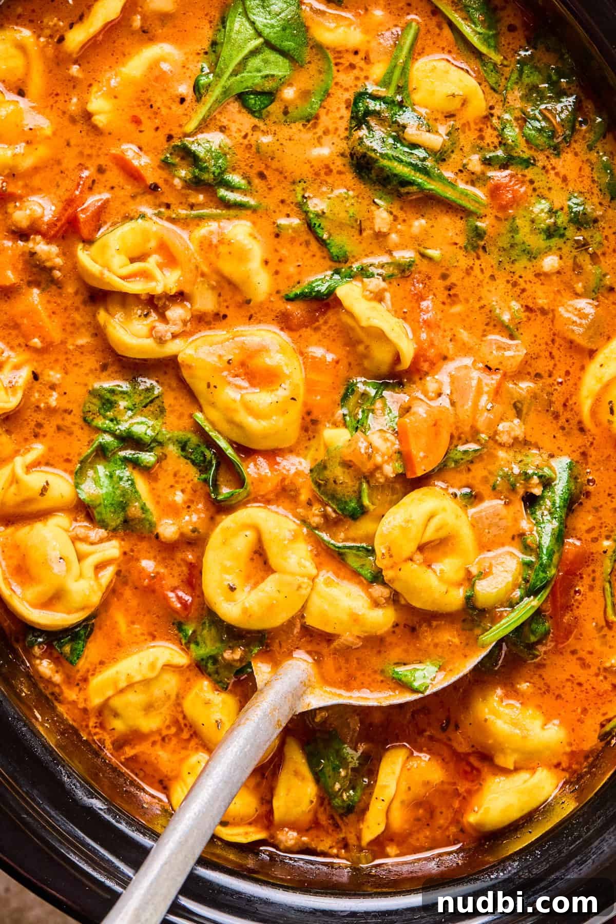 Slow-Cooker Sausage and Tortellini Soup Recipe 13 Crockpot with tomato based soup with sausage and tortellini and ladle spooning soup.