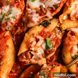 Ground beef stuffed shells in marinara with cheese and chopped basil over top.
