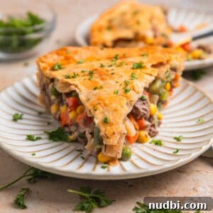 Slice of beef pot pie on plate topped with chopped parsley.