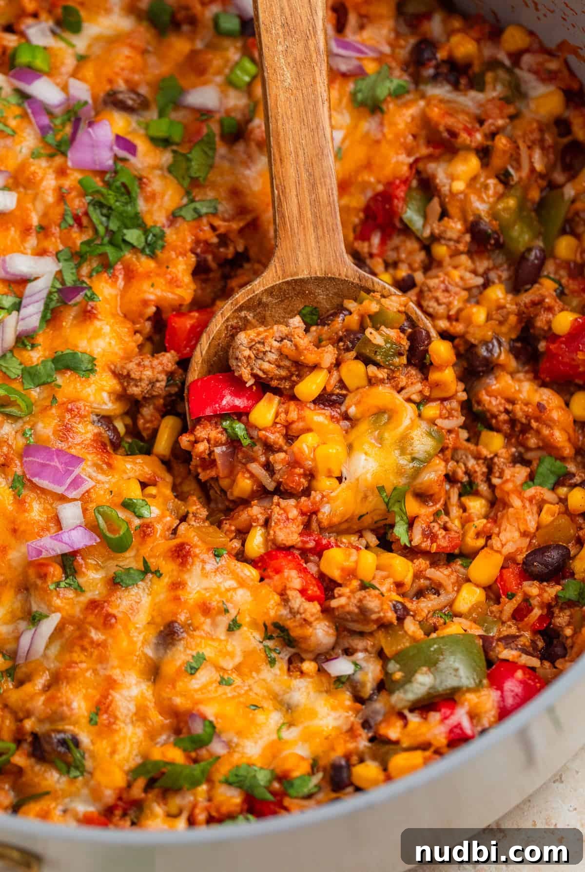 Cheesy Turkey Taco Skillet Dinner Recipe 11 Wood spoon scooping into skillet with turkey and rice mixture topped with melted cheese.