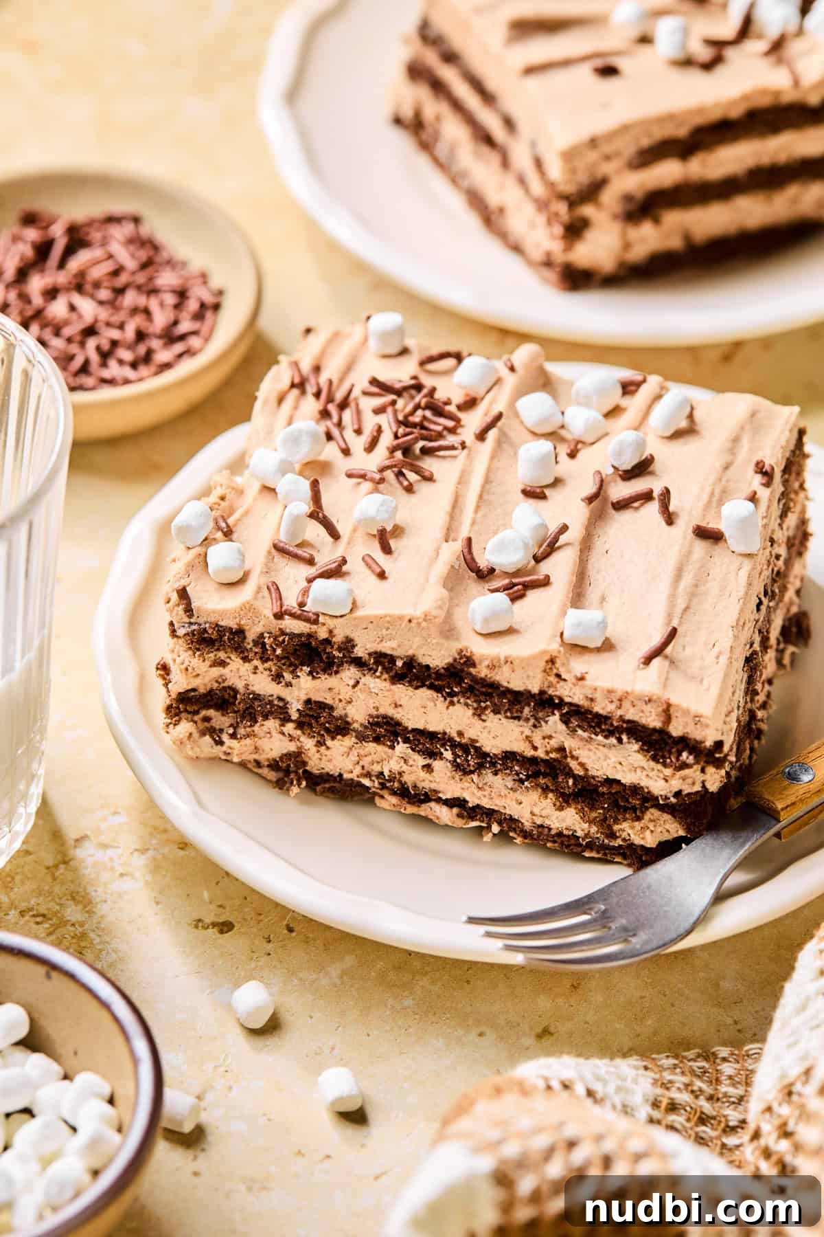 Decadent No-Bake Chocolate Icebox Cake Recipe 2 Hot chocolate icebox cake slice on plate with fork topped with chocolate sprinkles and marshmallows.