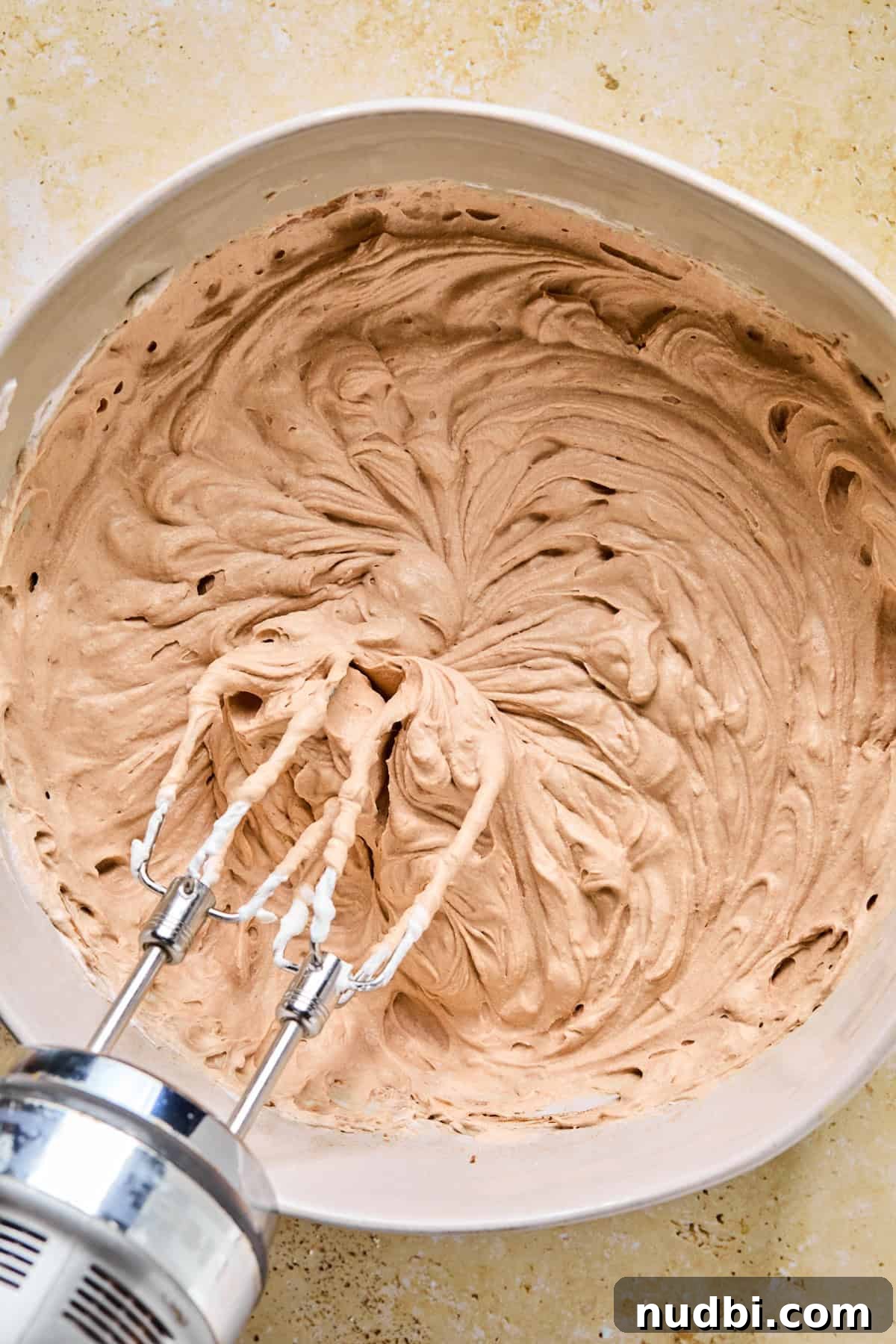 Decadent No-Bake Chocolate Icebox Cake Recipe 9 Chocolate whipped cream mixture in bowl with electric mixer propped above.