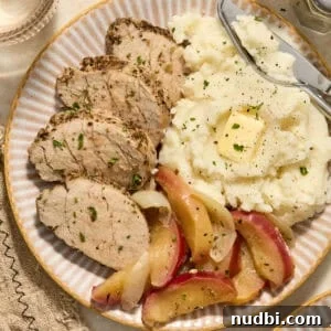 Pork tenderloin sliced on plate with apples and mashed potatoes.