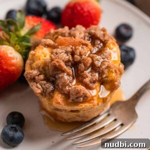 Baked French toast muffin with streusel topping on plate with maple syrup poured over top.