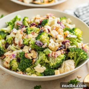 Broccoli cauliflower salad in bowl tossed with cheese, cranberries, bacon and more.
