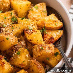 Parmesan roasted potatoes in serving dish with spoon topped with chopped fresh parsley and freshly grated parmesan.