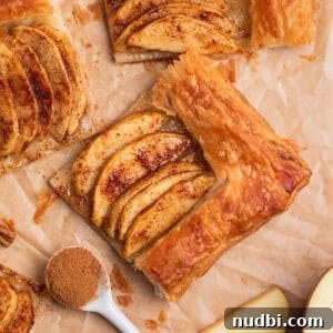 Overhead view of apple tarts on parchment with spoonful of cinnamon beside.