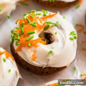 Carrot cake donut with cream cheese icing topped with sprinkles and shredded carrots.