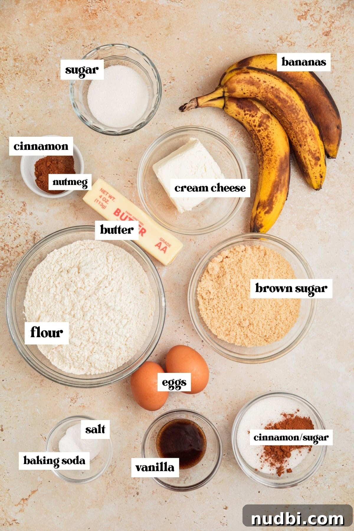 Moist Cinnamon Banana Bread Recipe with Warm Spice Flavor 4 Brown bananas, flour, butter, sugar and other labeled ingredients on surface.