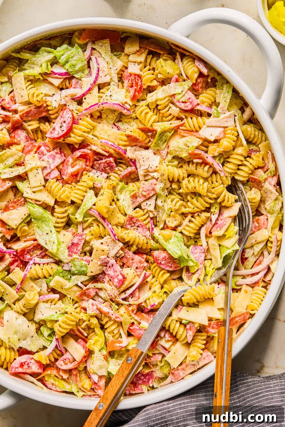 Italian Grinder Pasta Salad Recipe for Perfect Picnic Meals 2 Bowl with grinder pasta salad and serving utensils propped in the bowl.