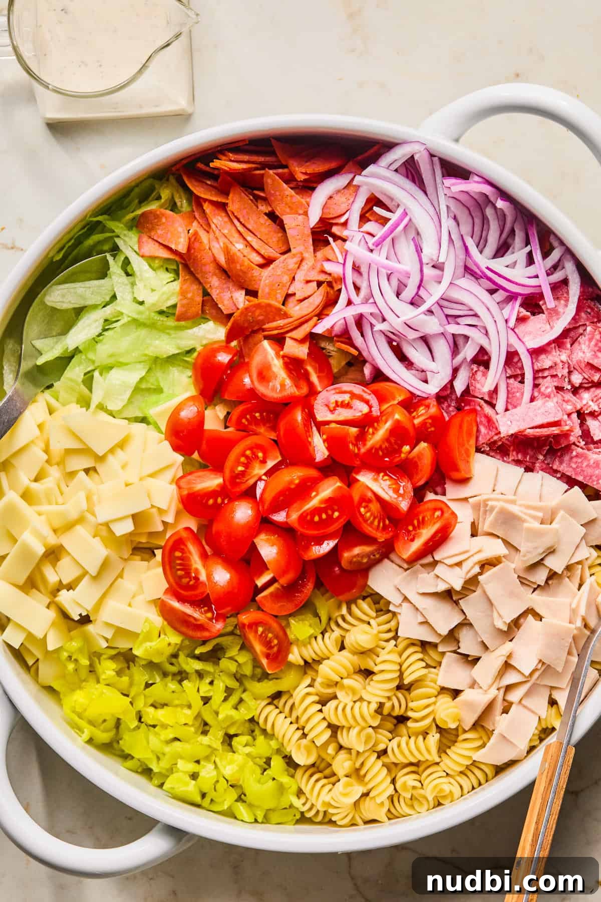 Italian Grinder Pasta Salad Recipe for Perfect Picnic Meals 5 Pasta, lettuce, banana peppers, provolone and other pasta salad ingredients in bowl.