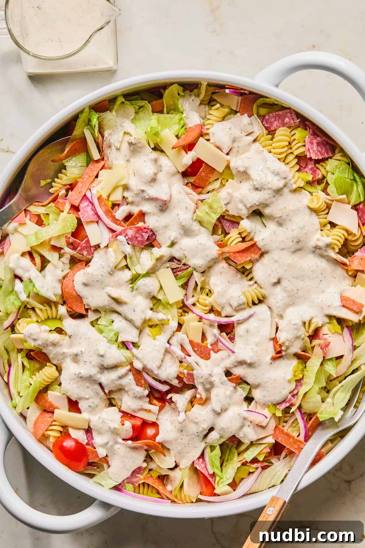 Italian Grinder Pasta Salad Recipe for Perfect Picnic Meals 9 Grinder pasta salad in bowl with dressing poured over top.