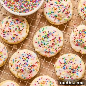 Iced Sugar Cookie Recipe: Soft, Chewy Cookies with Royal Icing 14 Iced sugar cookies on wire rack with sprinkles.