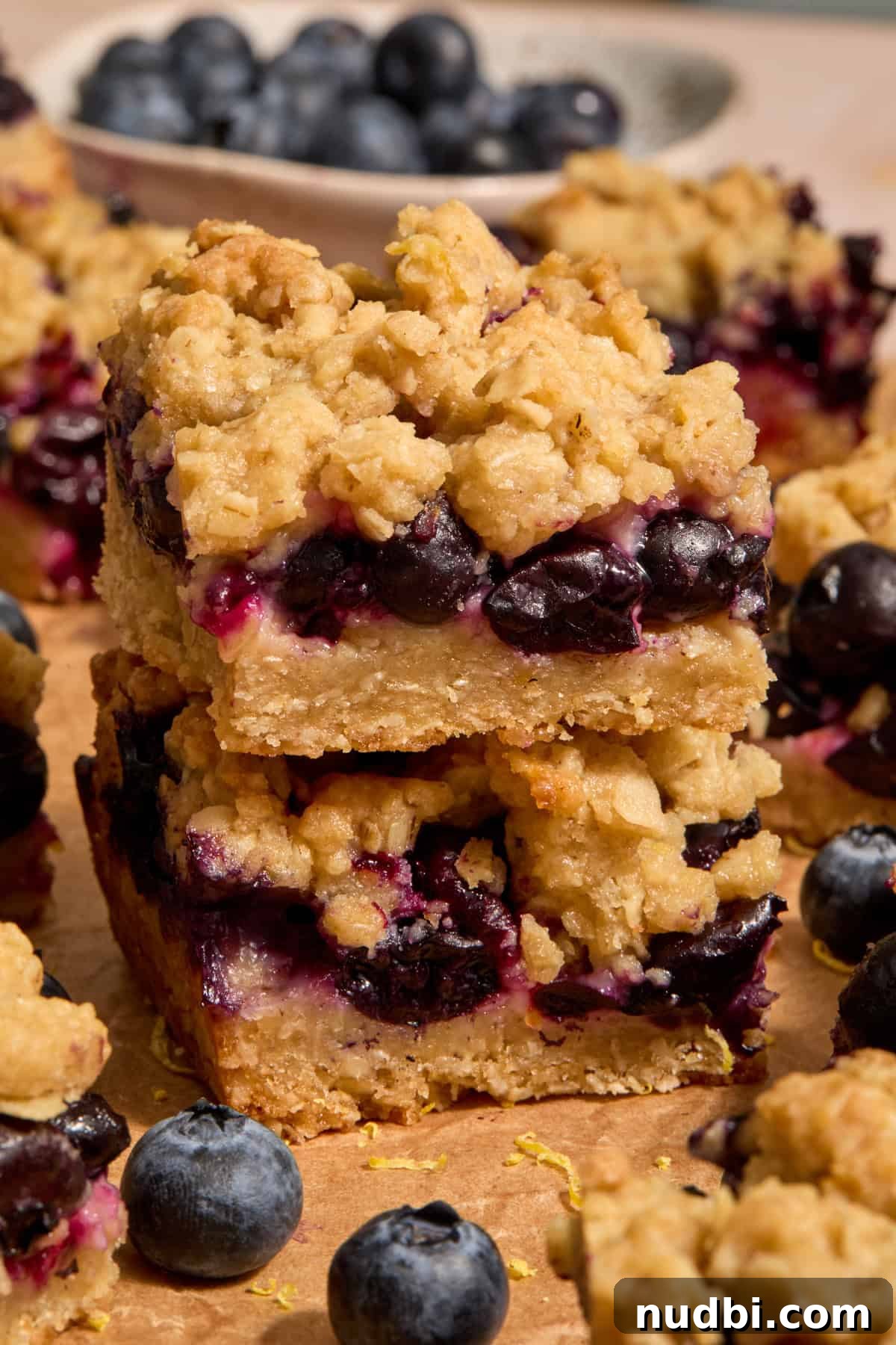Blueberry lemon bars stacked on parchment with berries surrounding.