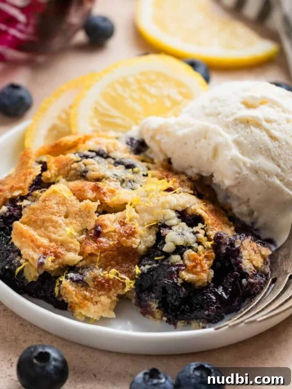 Blueberry lemon dump cake on white plate with fork and scoop of vanilla ice cream.