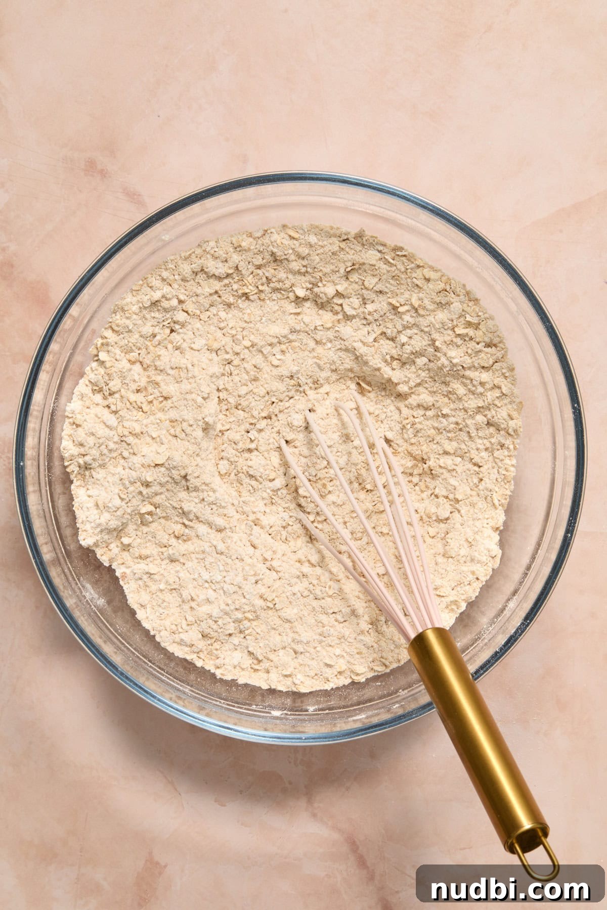 Whisked oats, brown sugar, flour and other ingredients in bowl with whisk.