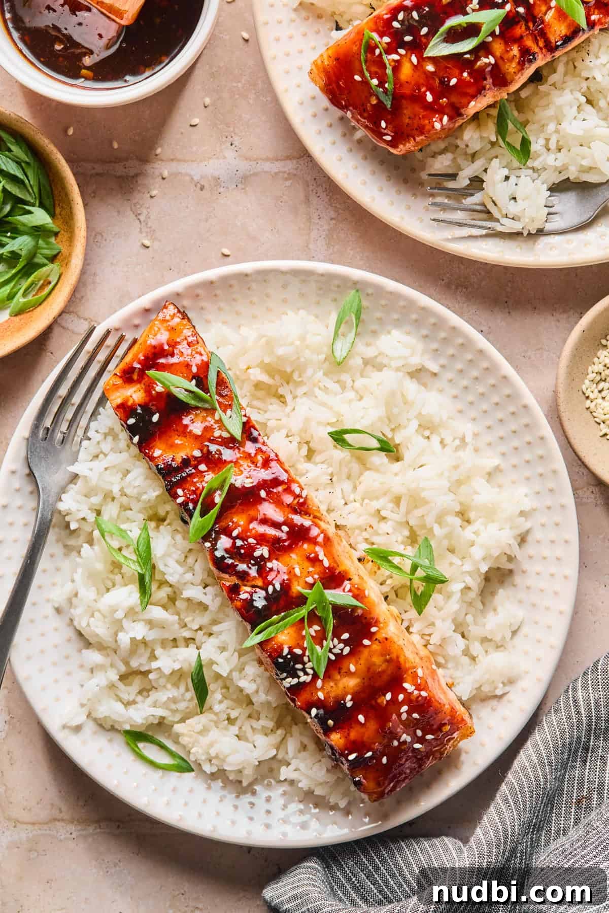 Crispy Grilled Teriyaki Salmon with Sticky Glaze Recipe 2 Teriyaki grilled salmon over bed of rice with sliced green onions and sesame seeds.