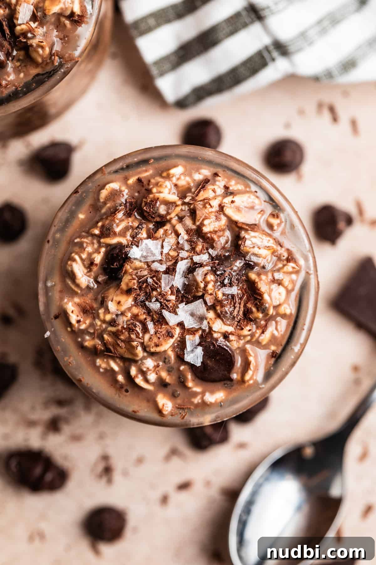 Triple Chocolate Overnight Oats Recipe for Chocolate Lovers 3 Overhead view of jar with chocolate oatmeal topped with coarse sea salt and spoon and chocolate chips surrounding.