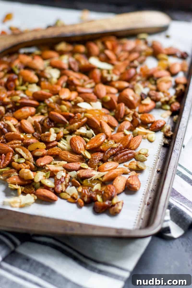 Maple Roasted Trail Mix Recipe with Nuts & Seeds 3 Sheet pan with trail mix with roasted nuts and raisins on parchment with spoon.