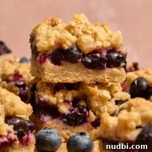 Stacked blueberry lemon bars with blueberries and other bars around it.