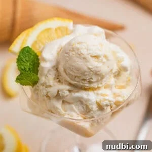 Scooped lemon ice cream in stemware with two lemon quarters and fresh mint leaves.