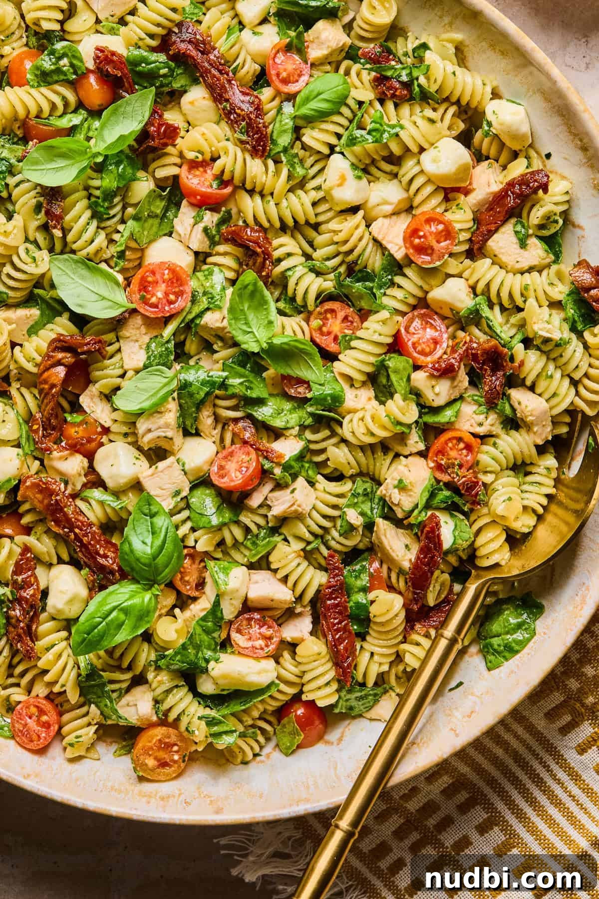 Pesto Chicken Pasta Salad with Sun-Dried Tomatoes and Basil 2 Pesto chicken pasta salad in bowl with serving spoon.