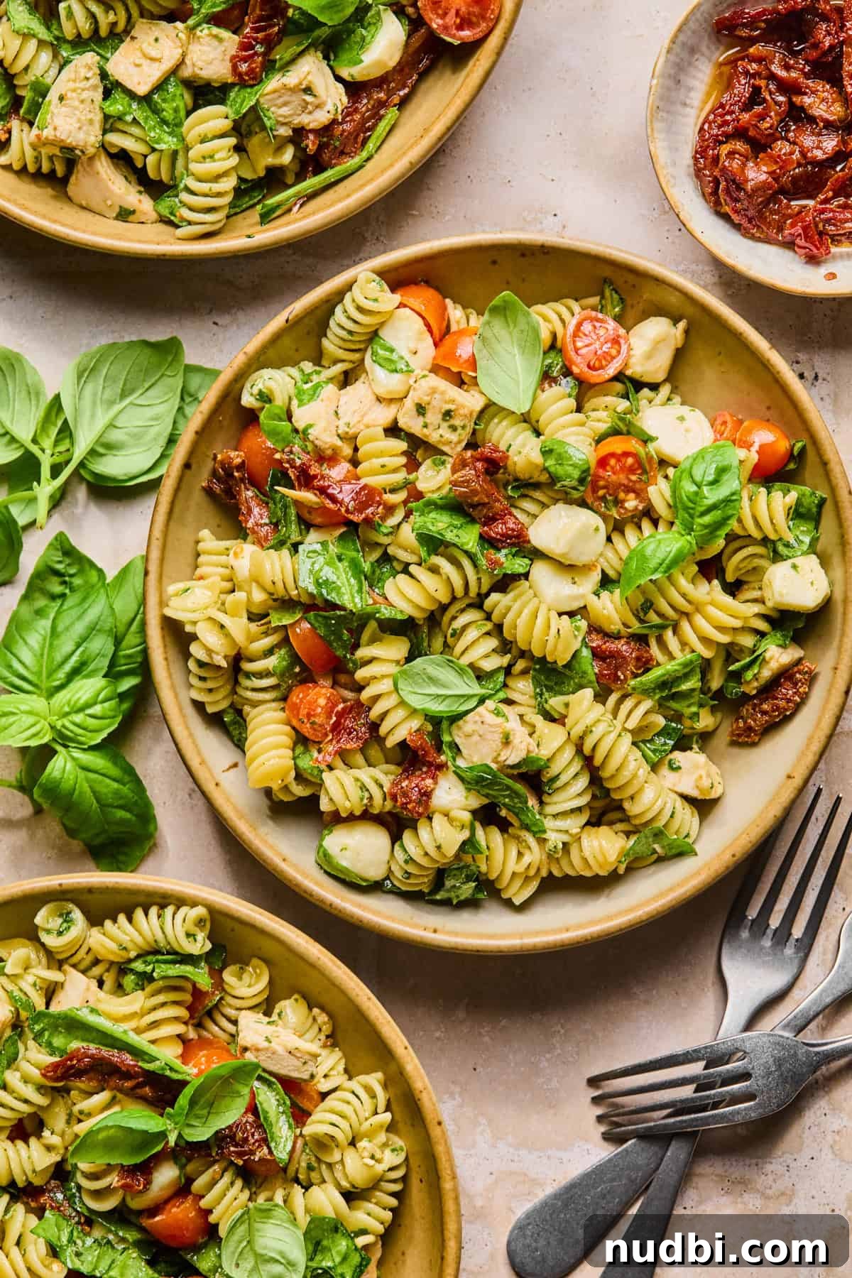Pesto Chicken Pasta Salad with Sun-Dried Tomatoes and Basil 11 Bowls with pesto pasta salad with chicken and forks.