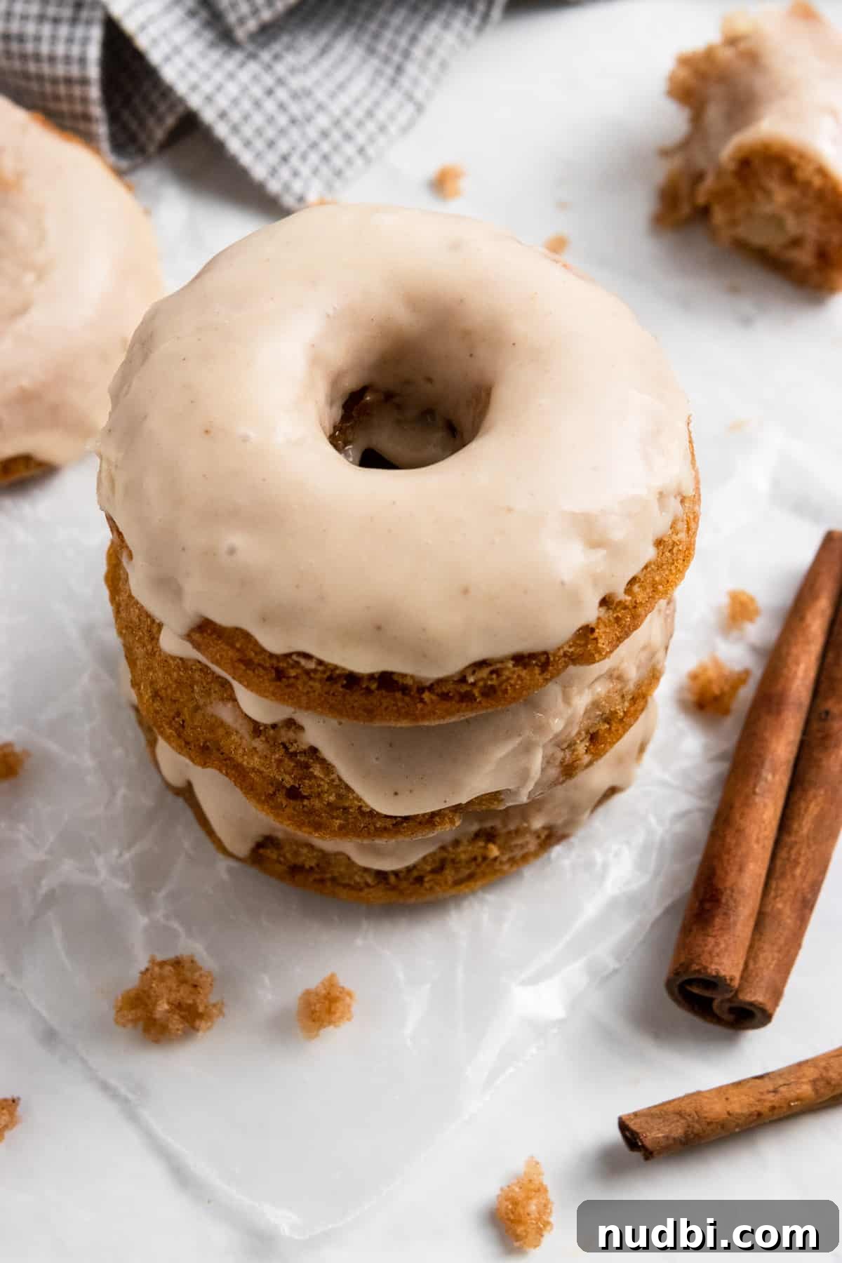 Apple Cider-Glazed Apple Cinnamon Donuts Recipe 2 Baked apple donuts stacked with glaze and cinnamon sticks.