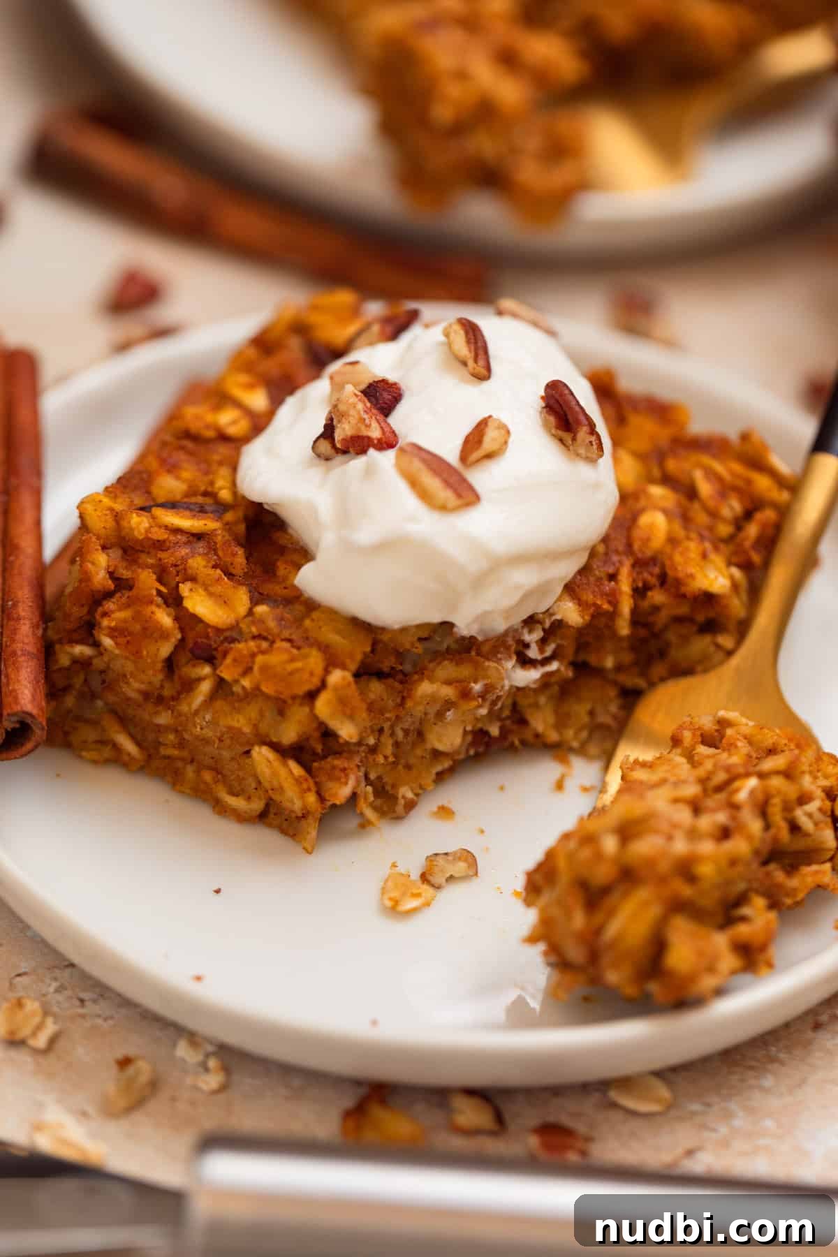 Baked pumpkin oat meal on white plate with greek yogurt and pecans on top.