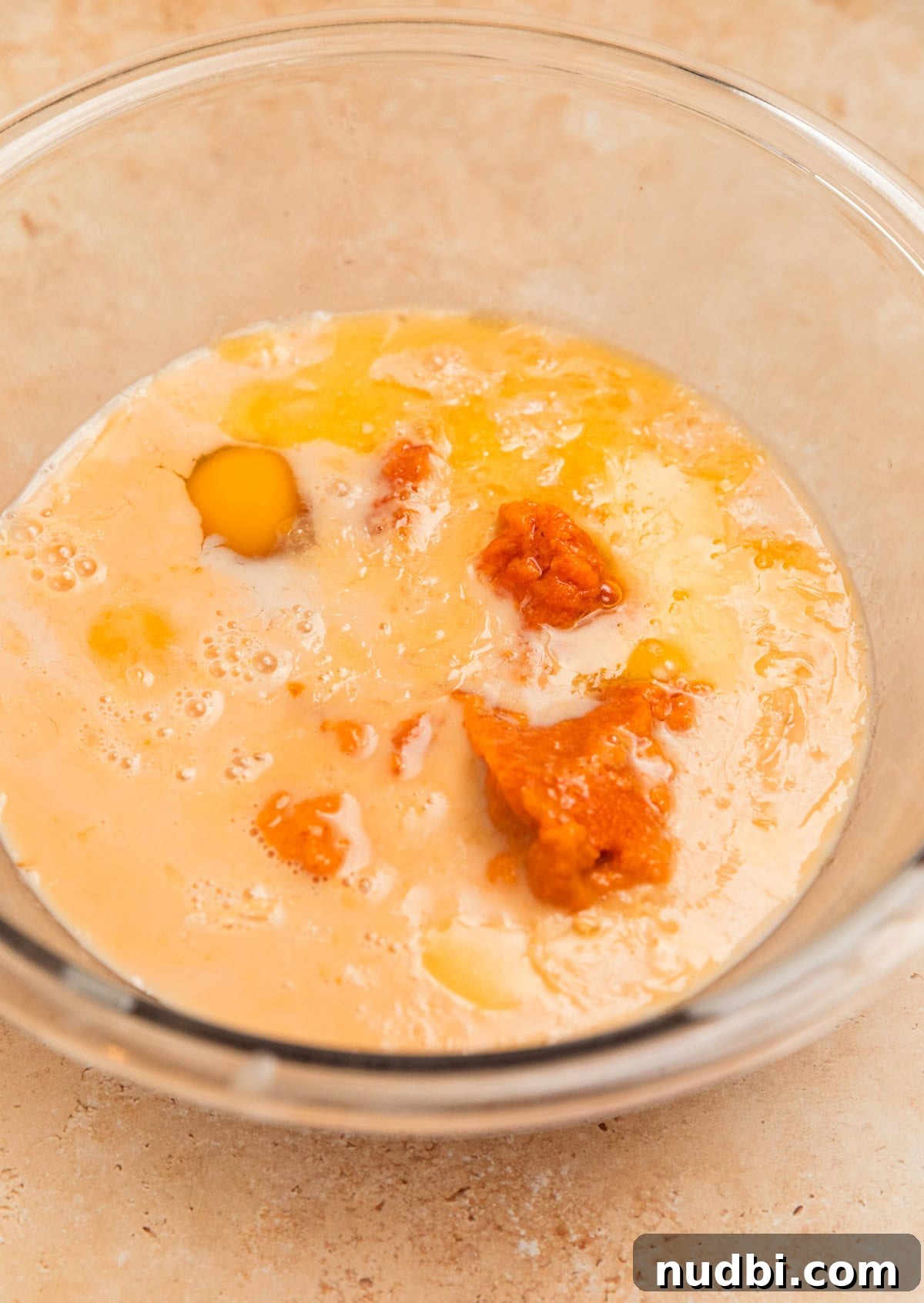 Milk, pumpkin, eggs and maple syrup in glass mixing bowl.