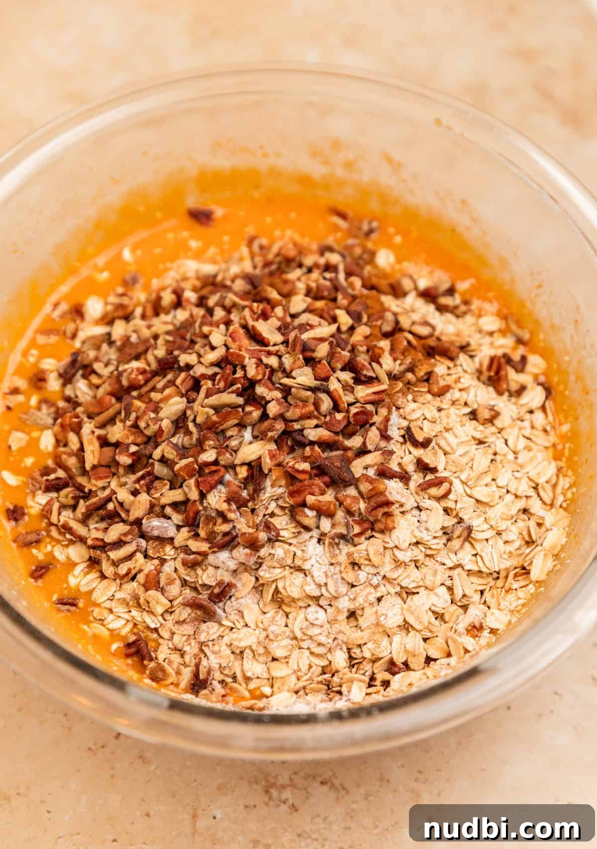 Rolled oats and pecans added to wet ingredients in bowl.