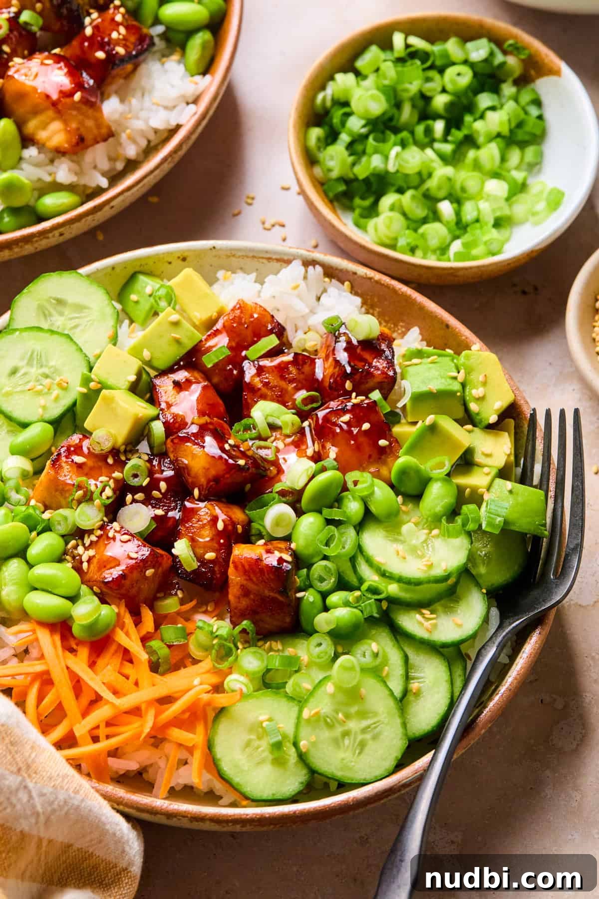 Teriyaki Salmon Rice Bowl with Scallions and Sesame 11 Teriyaki salmon cubes in rice bowls with cucumbers, carrots and green onion.