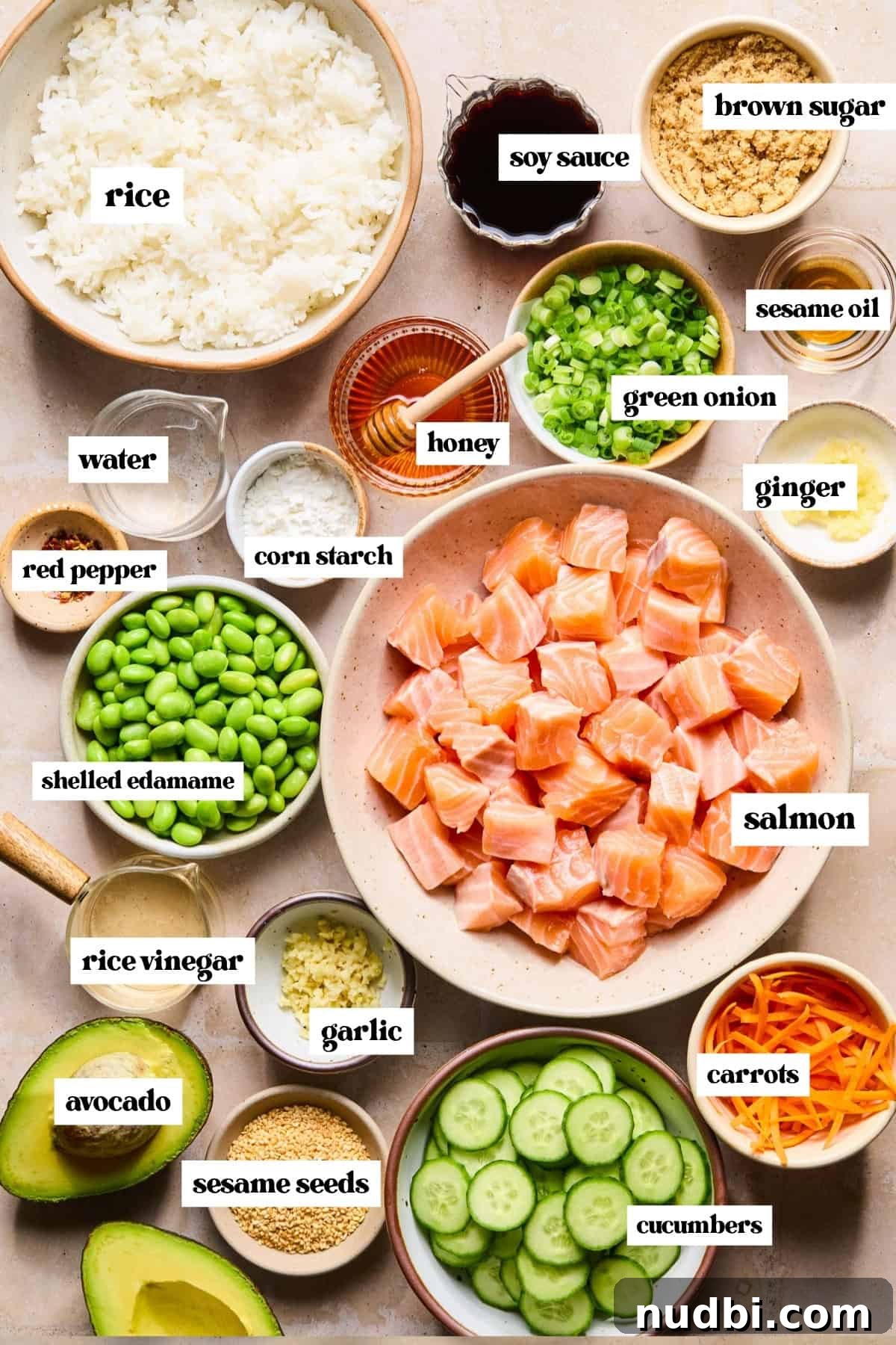 Teriyaki Salmon Rice Bowl with Scallions and Sesame 4 Cubed salmon in bowl, vegetables, soy sauce, rice and other labeled ingredients on surface.