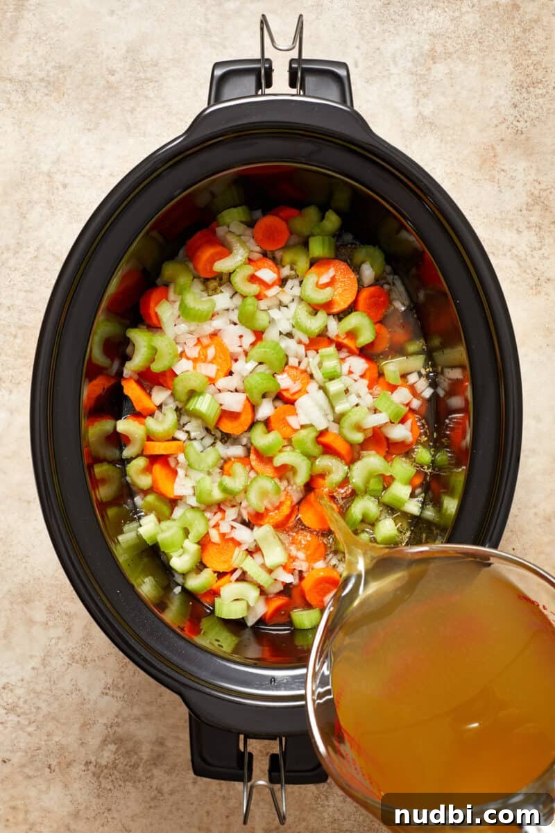Slow-Cooker Chicken and Wild Rice Soup Recipe 5 Celery, onion and carrots in slow cooker pot with broth being poured over.