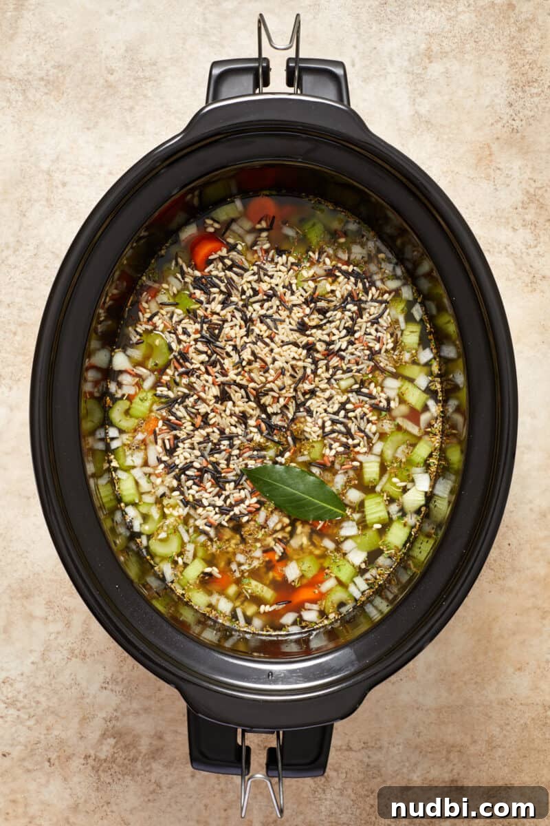 Slow-Cooker Chicken and Wild Rice Soup Recipe 6 Chicken and wild rice soup ingredients in slow cooker before cooked with bay leaf over top.