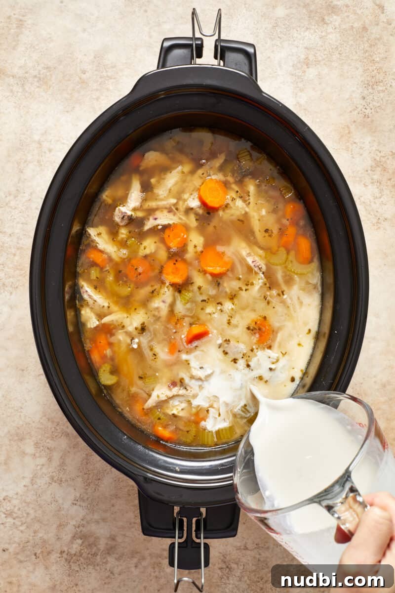 Slow-Cooker Chicken and Wild Rice Soup Recipe 8 Cream being added to chicken and rice soup in crock pot.