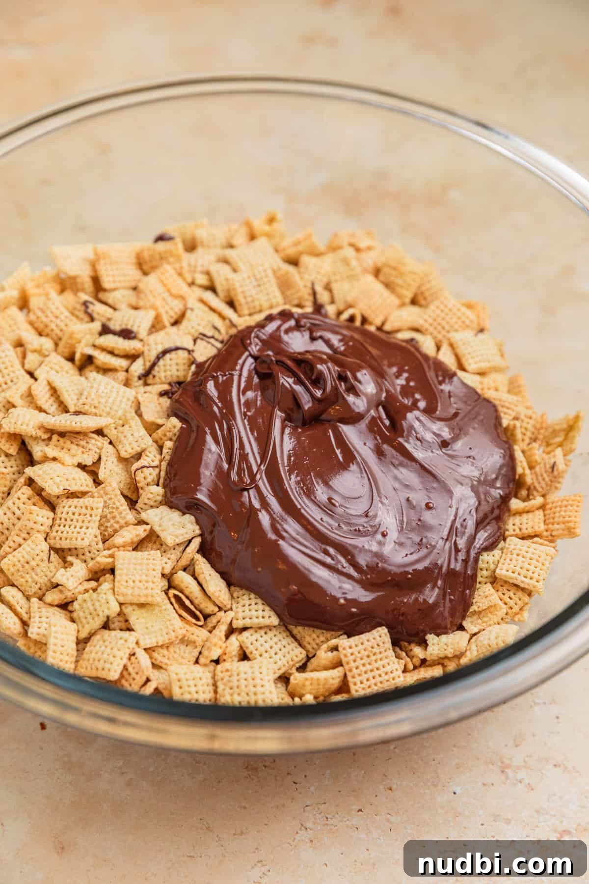 Christmas Puppy Chow Recipe: Festive Snack Mix for Holiday Parties 5 Melted chocolate added to chex cereal in glass bowl.