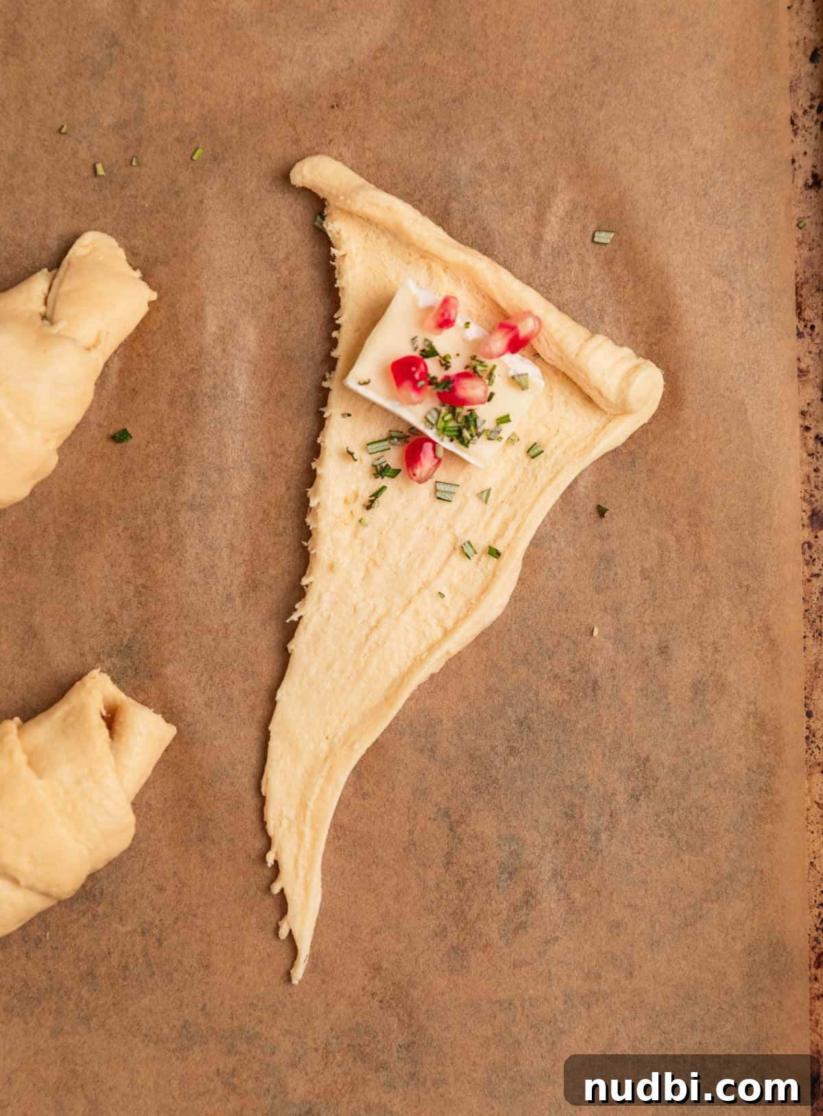 Baked Brie Crescent Rolls with Honey & Cranberry Jam 5 Crescent roll dough on parchment with brie, rosemary and pomegranate.