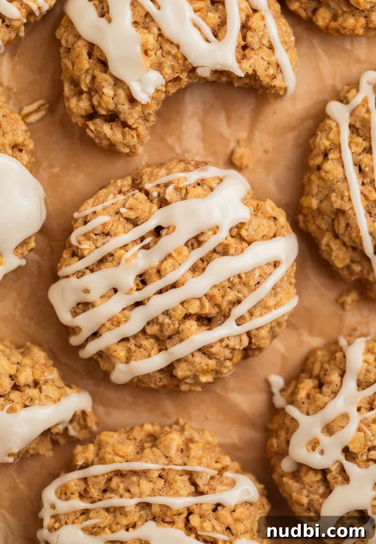 Cinnamon Roll Breakfast Cookies: Soft, Swirled Morning Treats 2 Cinnamon oatmeal cookies with icing drizzle on parchment.