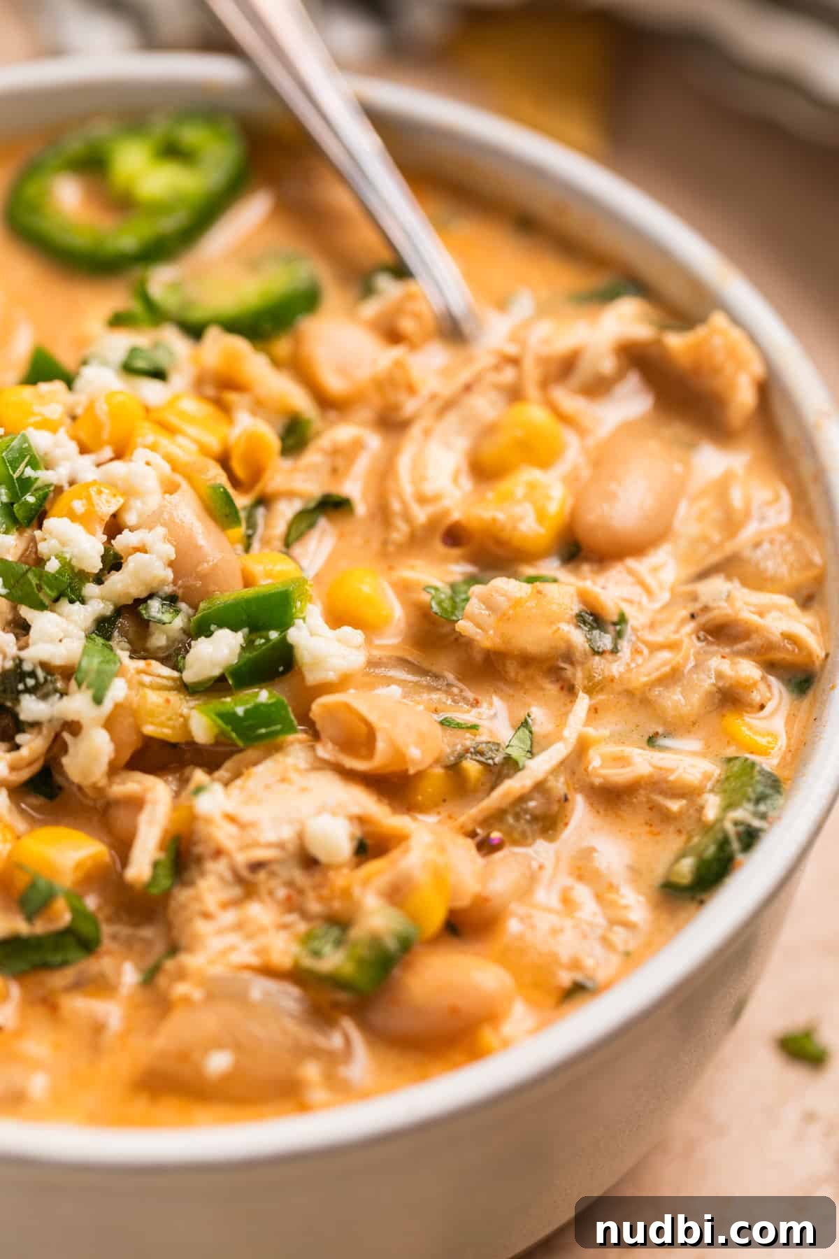 Creamy Slow Cooker White Chicken Chili Recipe 13 Bowl of crock pot white chicken chili with spoon and topped with corn, cilantro, cheese and jalapeño.