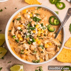 Creamy Slow Cooker White Chicken Chili Recipe 14 White bowl with white chicken chili with toppings and spoon.
