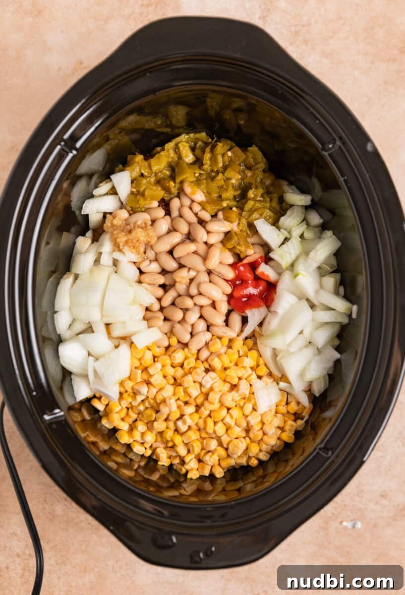 Creamy Slow Cooker White Chicken Chili Recipe 5 Corn, onion, green chiles, garlic and sriracha covering chicken in crockpot.