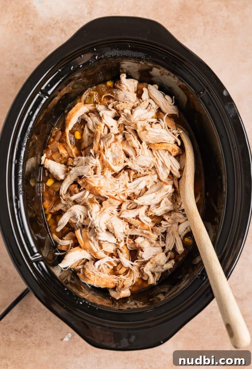 Creamy Slow Cooker White Chicken Chili Recipe 9 Chicken added to chili cooking in crockpot with wood spoon