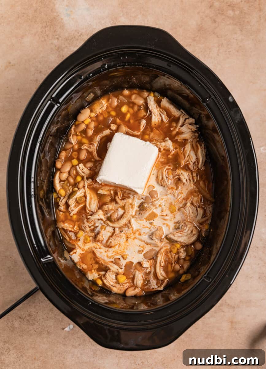 Creamy Slow Cooker White Chicken Chili Recipe 10 Cream cheese block added to crock pot with white chicken chili.