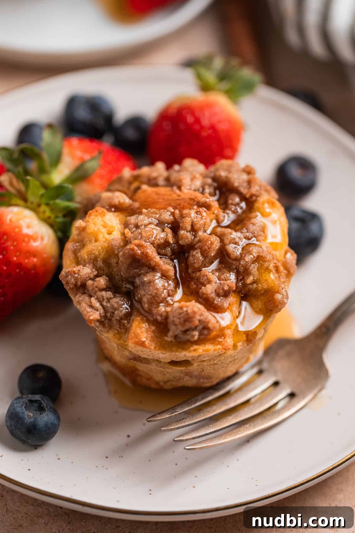 Cinnamon French Toast Muffins: Quick Breakfast Muffin Recipe 2 Baked French toast muffin with streusel topping and maple syrup over top.