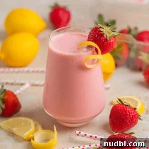 Refreshing Strawberry Lemonade Smoothie Recipe for Summer Sips 6 Wine glass with strawberry lemon smoothie with lemon zest and strawberry garnish and berries, lemon slices and straws surrounding.