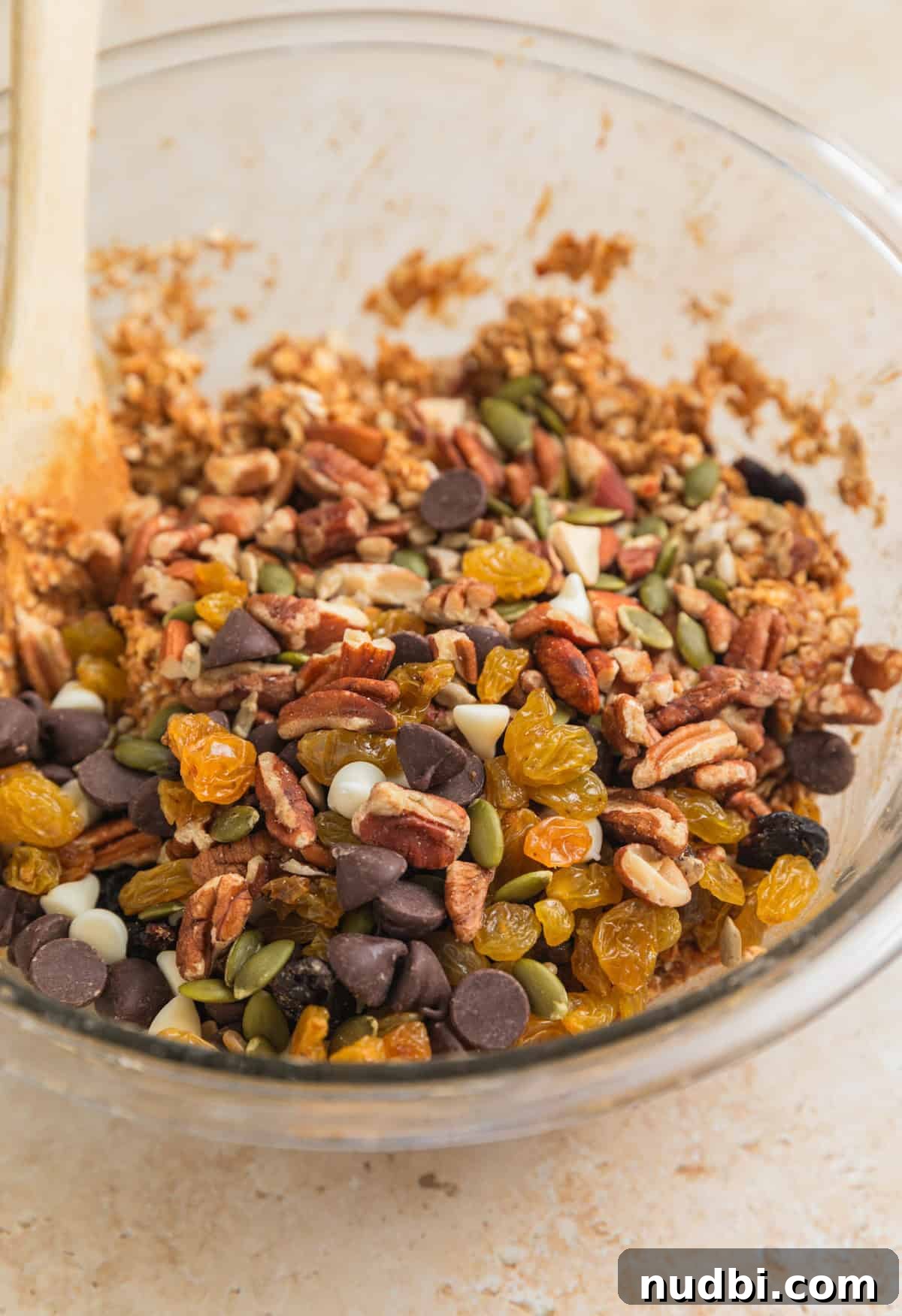 Homemade Trail Mix Bars Recipe – Portable Snack Bars for Hiking 8 Trail mix ingredients added over top of oatmeal mixture in bowl with wooden spoon.