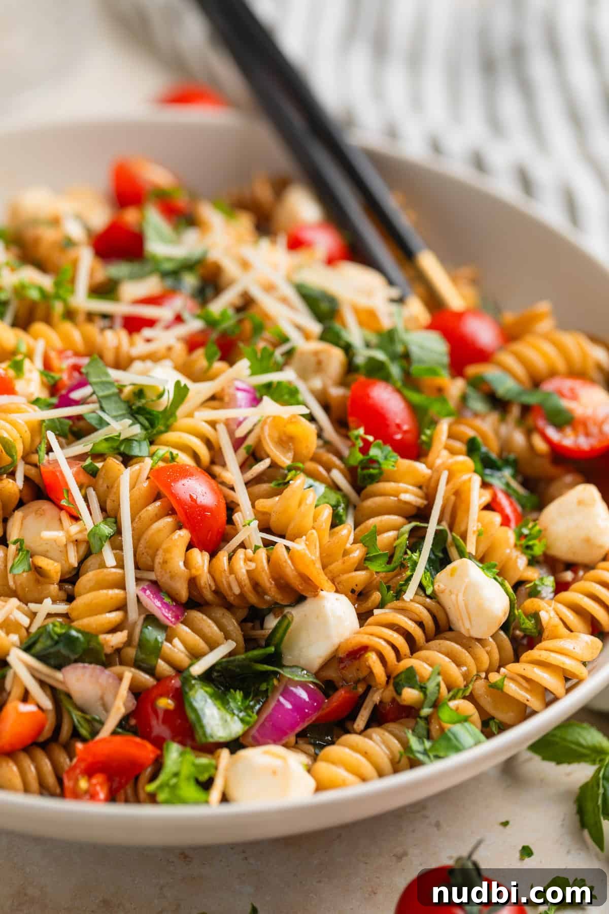 Tomato basil pasta salad with fresh mozzarella topped with chopped parsley in serving dish. 