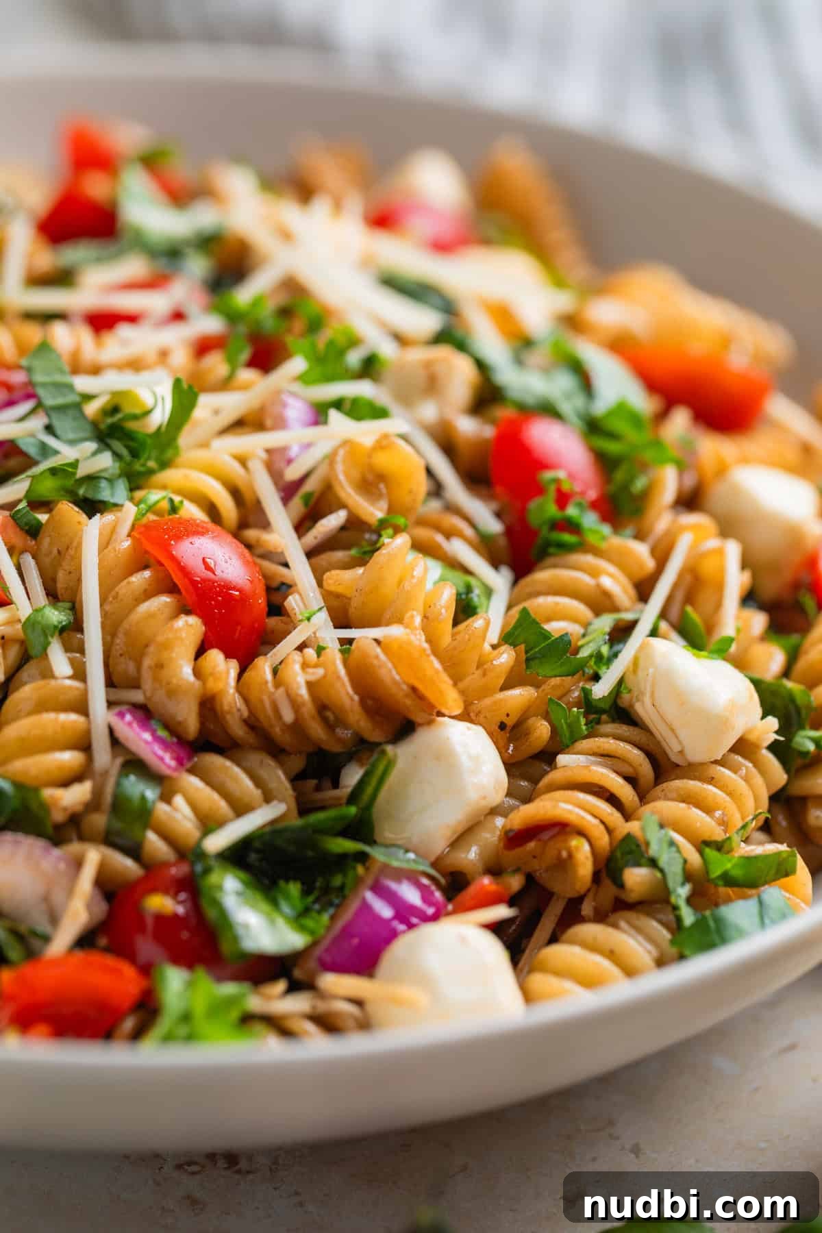 Close up view of tomato and basil rotini pasta salad topped with shredded parmesan and chopped basil.